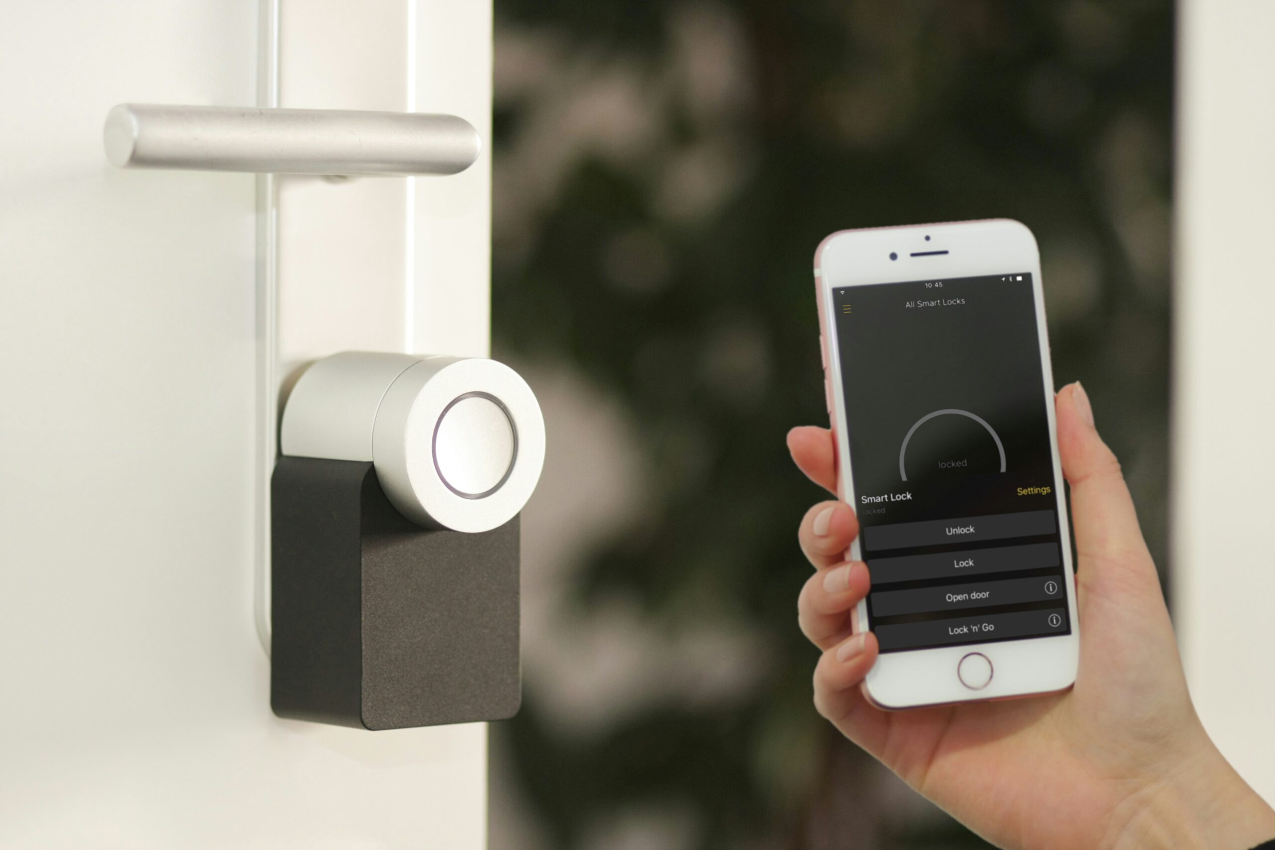 A person holds a smartphone displaying a smart lock app next to a modern door lock, showcasing smart home features like remote control and enhanced convenience.