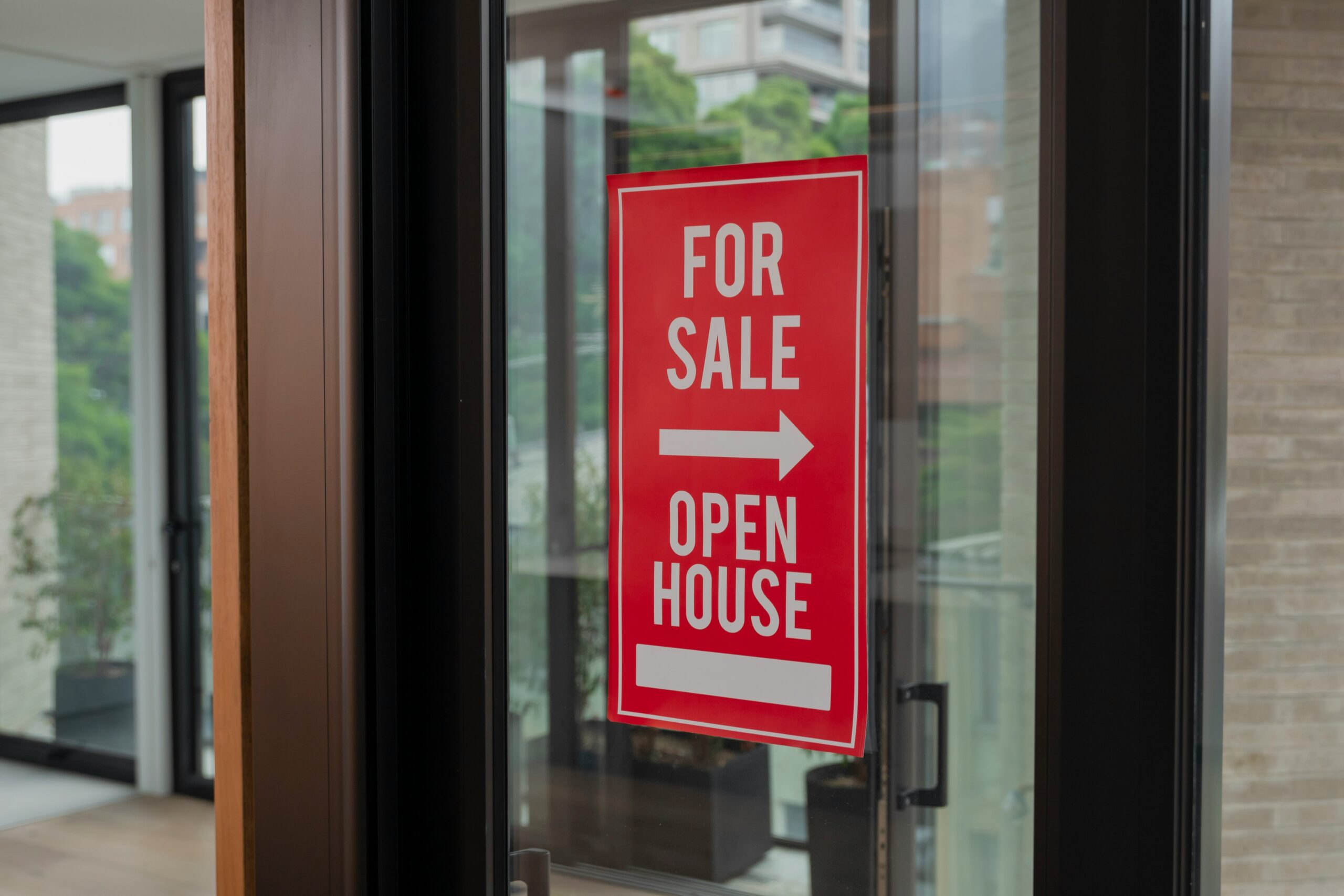 A red open house For Sale sign with a right arrow is posted on a glass door, indicating that a property inside is available for viewing and purchase.