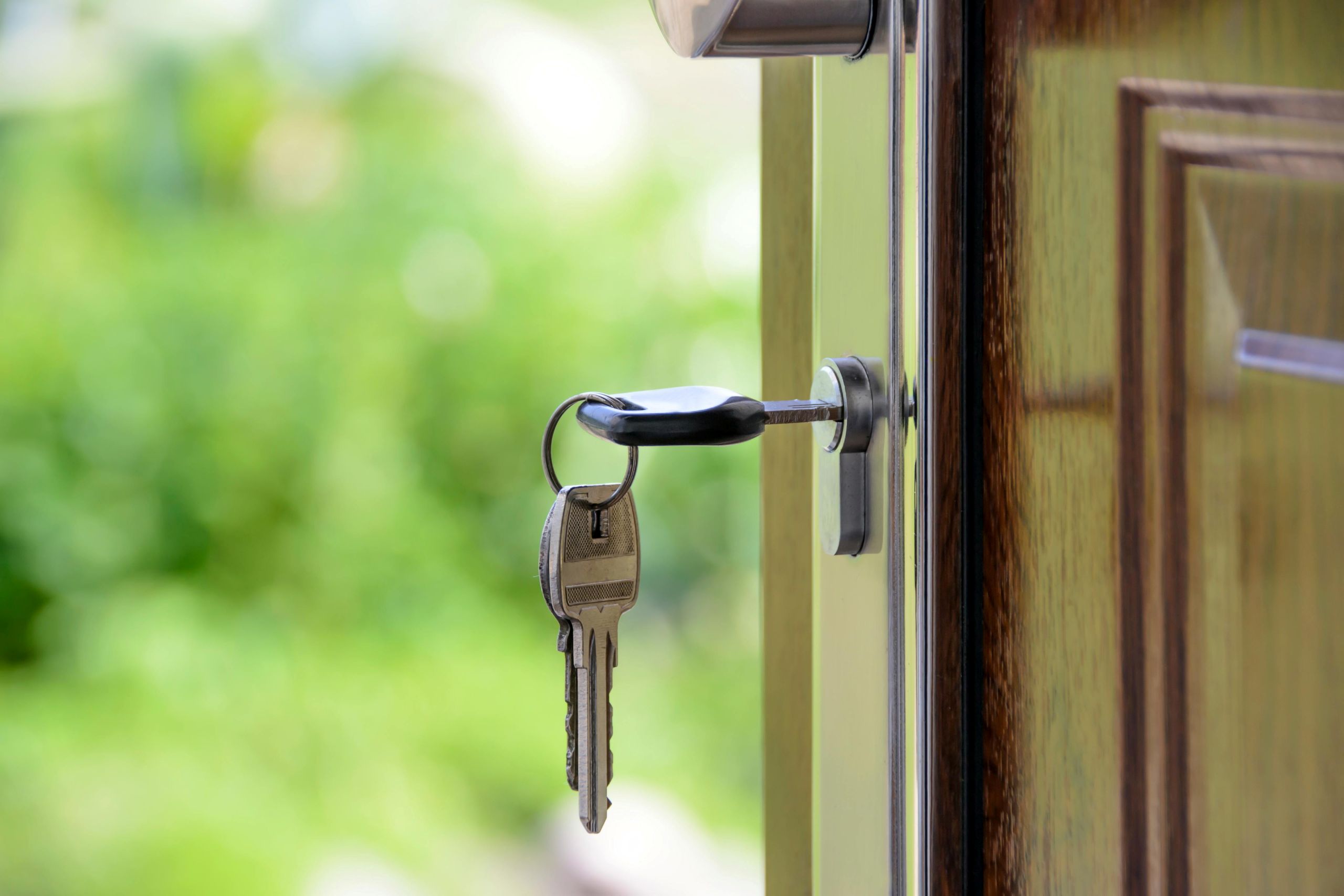 A set of keys dangling from a keyhole in a wooden door that is slightly open, with a blurred green outdoor background—a scene that hints at the best time to buy a house in Arkansas.