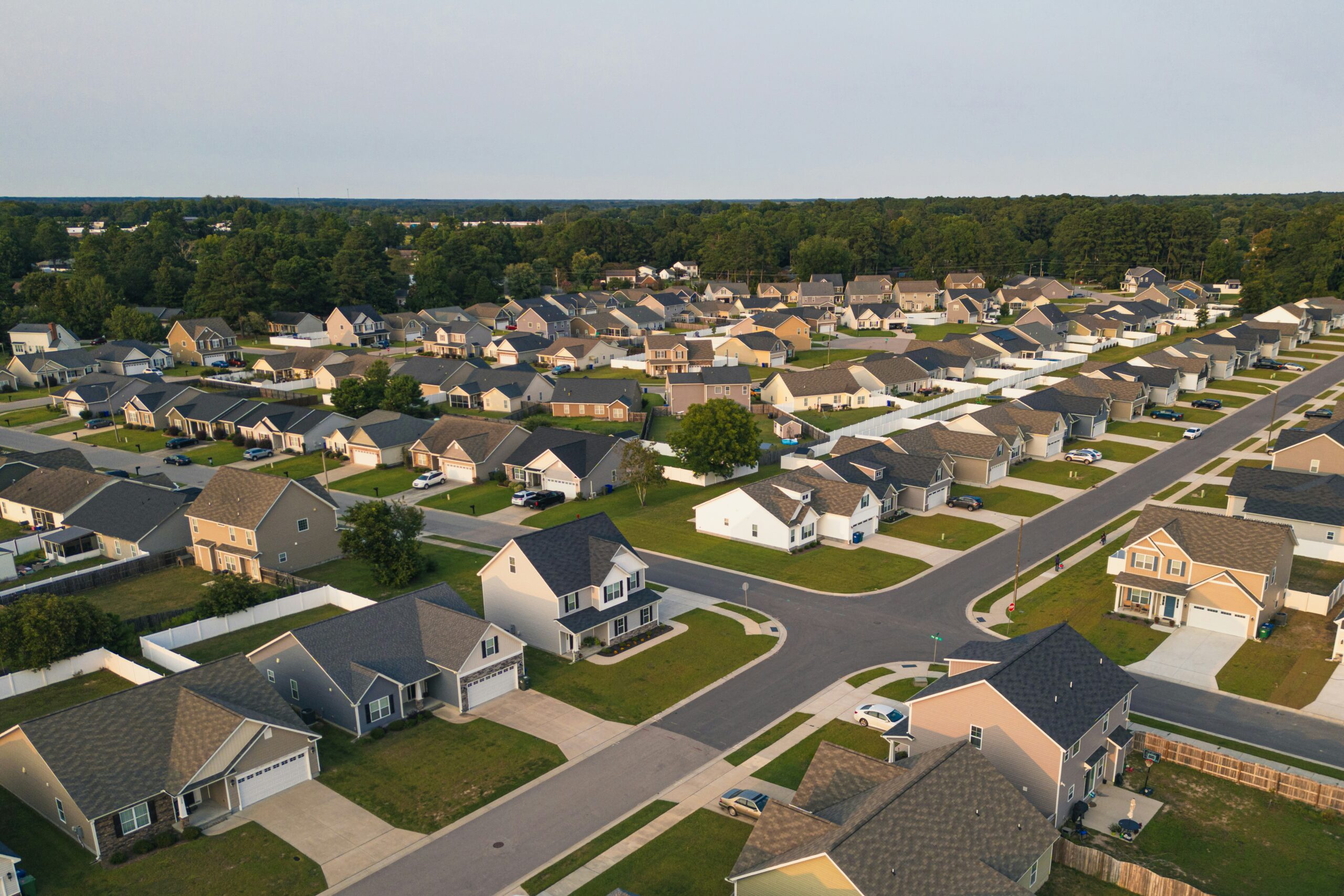 Aerial view of a suburban neighborhood with rows of houses, green lawns, streets, and trees in the background under a clear sky—capturing the inviting charm of living in Cabot AR.