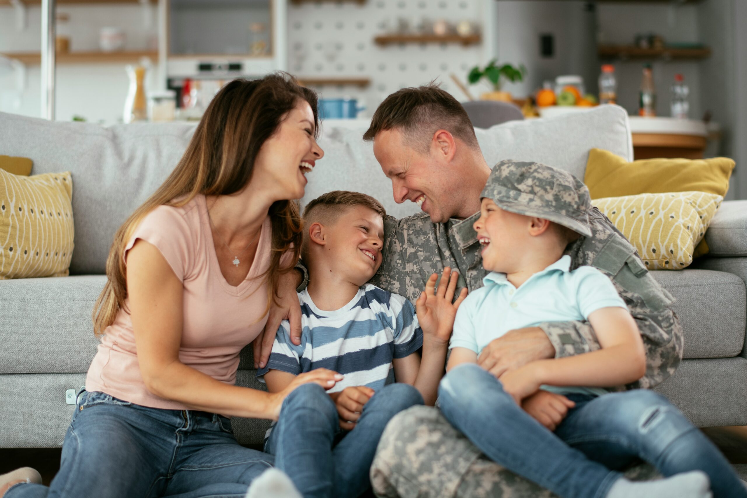 getty-images-FkInJvnvE2Q-unsplash A smiling family sits together on the couch— a woman, a man in military uniform, and two young boys laugh and hug, sharing a joyful moment at home as they celebrate their recent PCS to Little Rock Air Force Base.